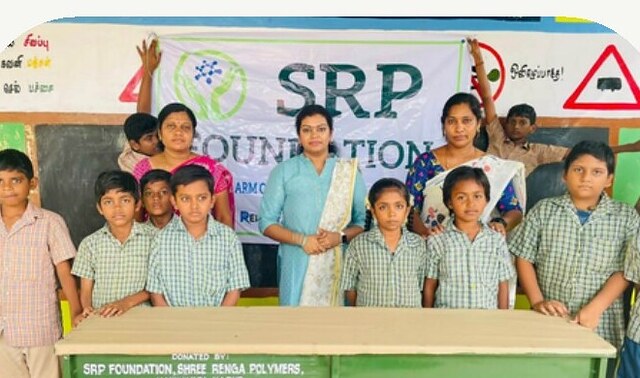 Schoolchildren stand with a new desk donated by SRP Foundation and Shree Renga Polymers, Kankkavadi, Karur.